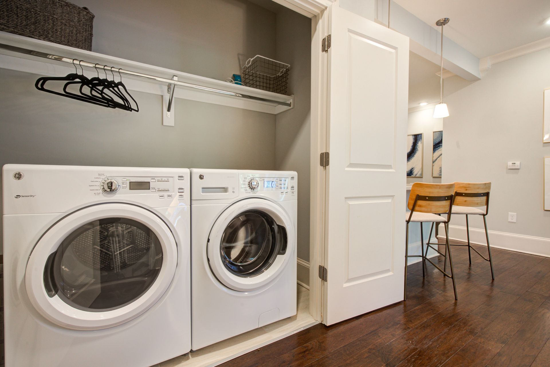 Laundry machines in a small closet; clothes hangers, shelves, and a door visible.