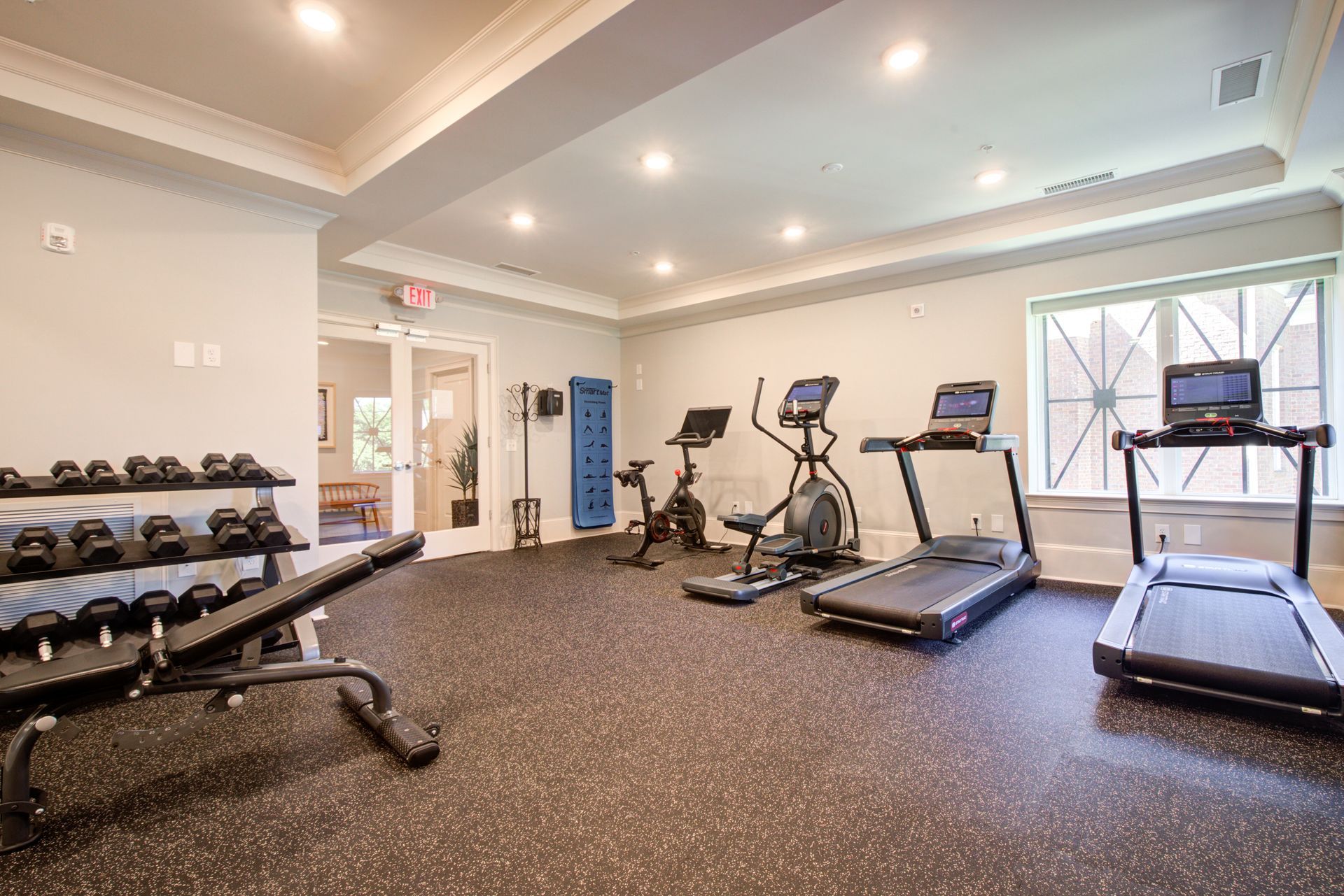 Gym with exercise equipment: dumbbells, bench, treadmill, elliptical, stationary bike.