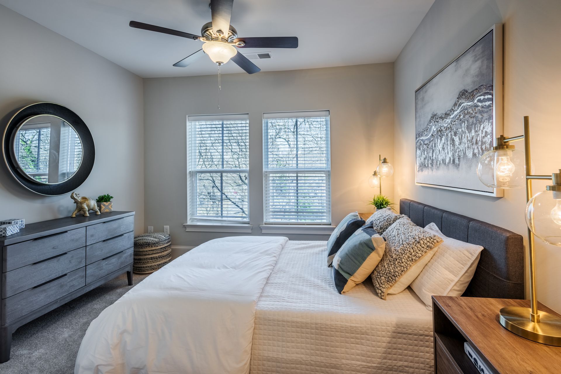 Bedroom with bed, dresser, window, mirror, and decorative lamps; neutral tones.