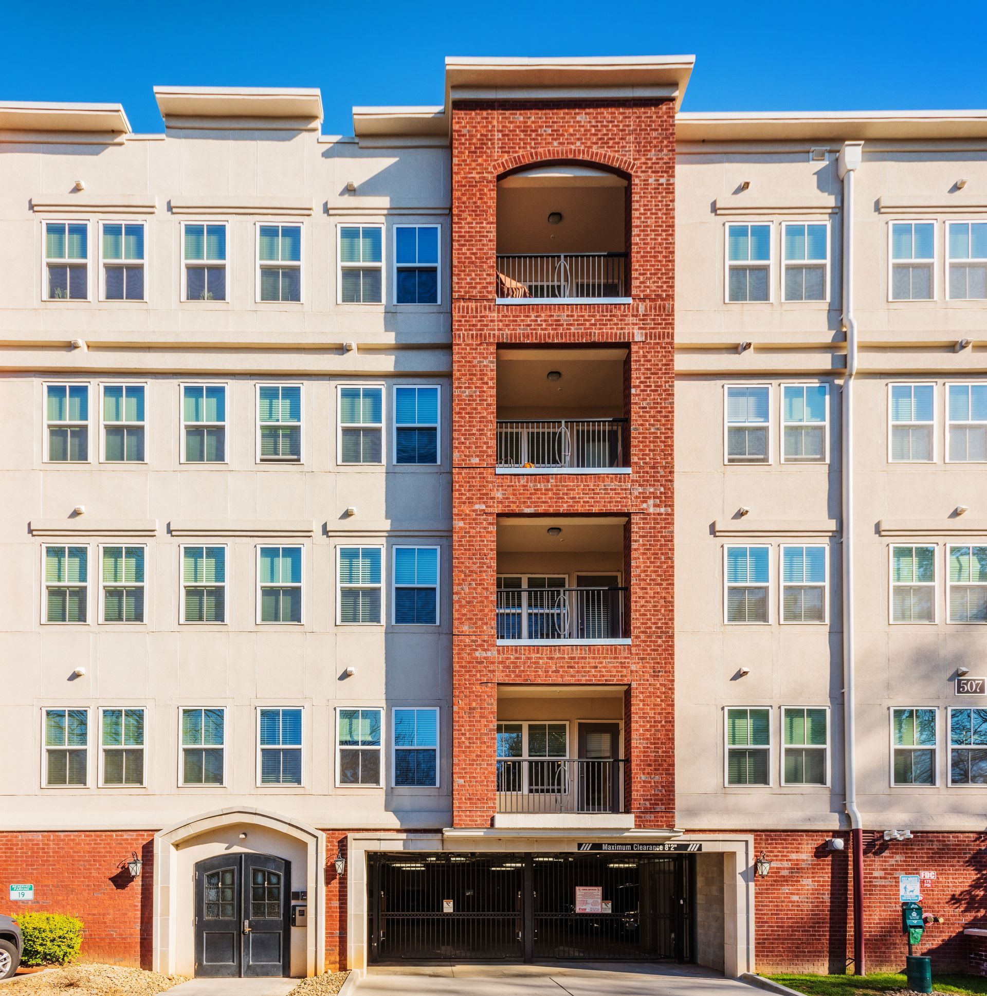 Multi-story apartment building with red brick accents and a parking garage entrance.