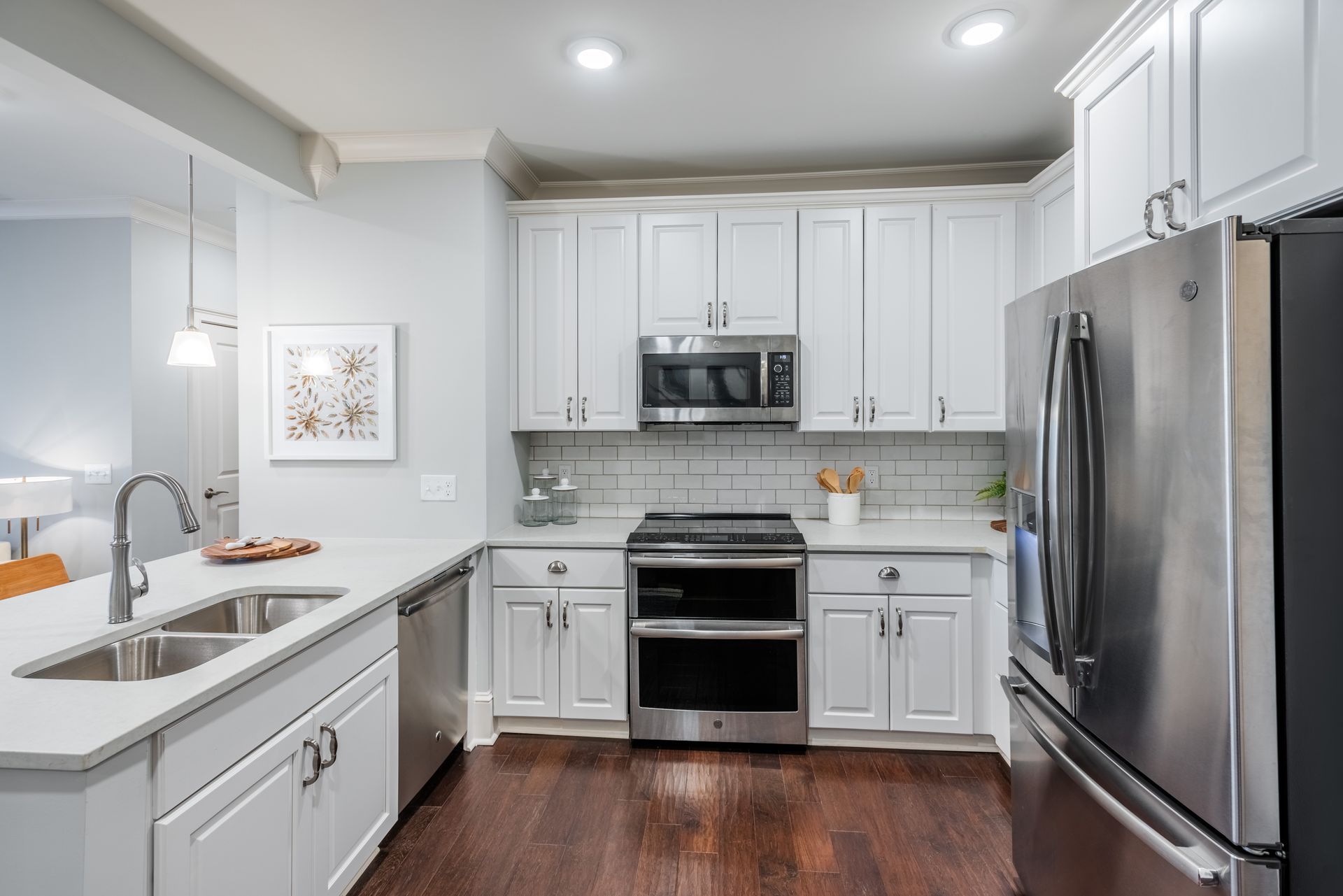 White kitchen with stainless steel appliances, white cabinets, light gray countertops, and dark wood floors.