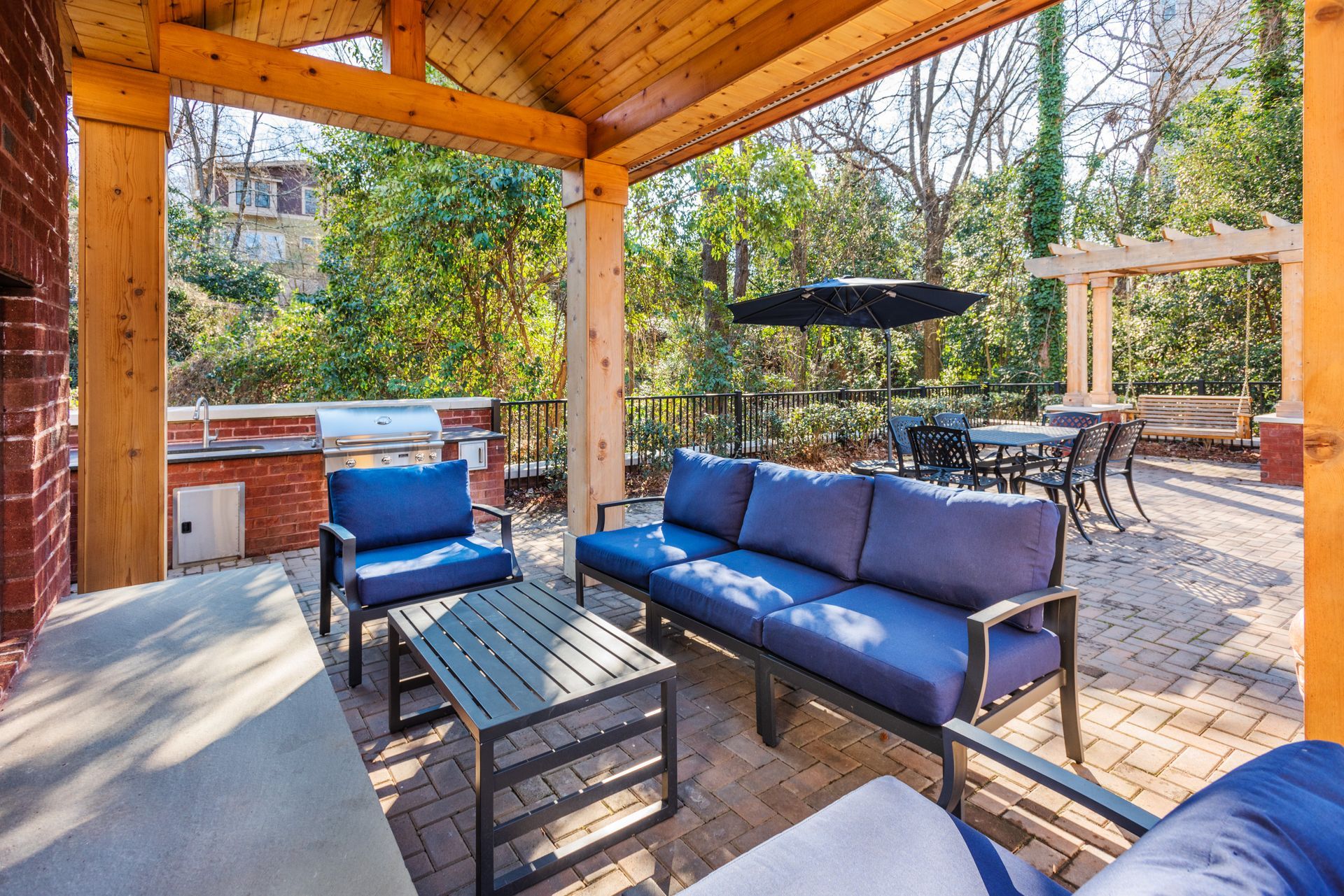 Outdoor patio with blue furniture, brick and wood construction, surrounded by greenery.