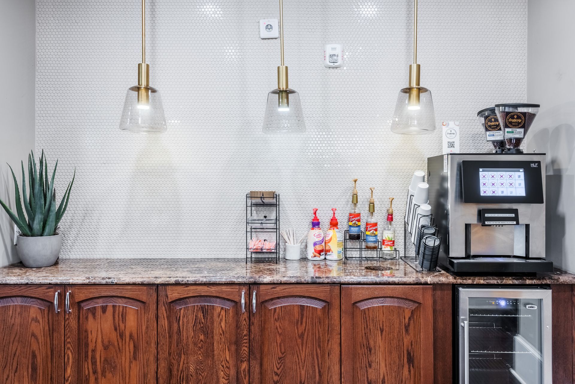 Coffee station with espresso machine, syrups, and glass pendant lights.