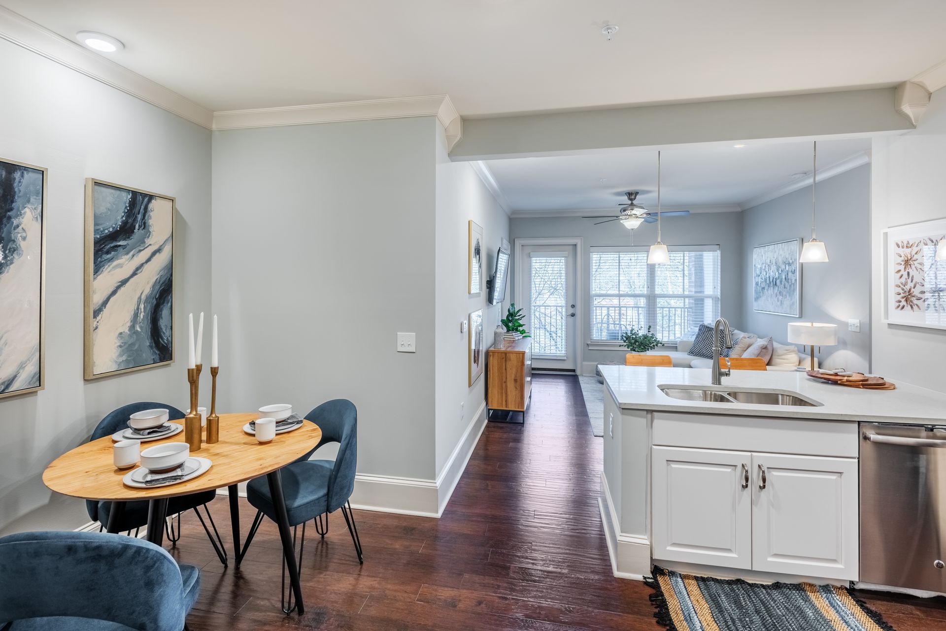 Open-plan living space with dining area, kitchen island, and view into living room. Soft blue walls, hardwood floors.