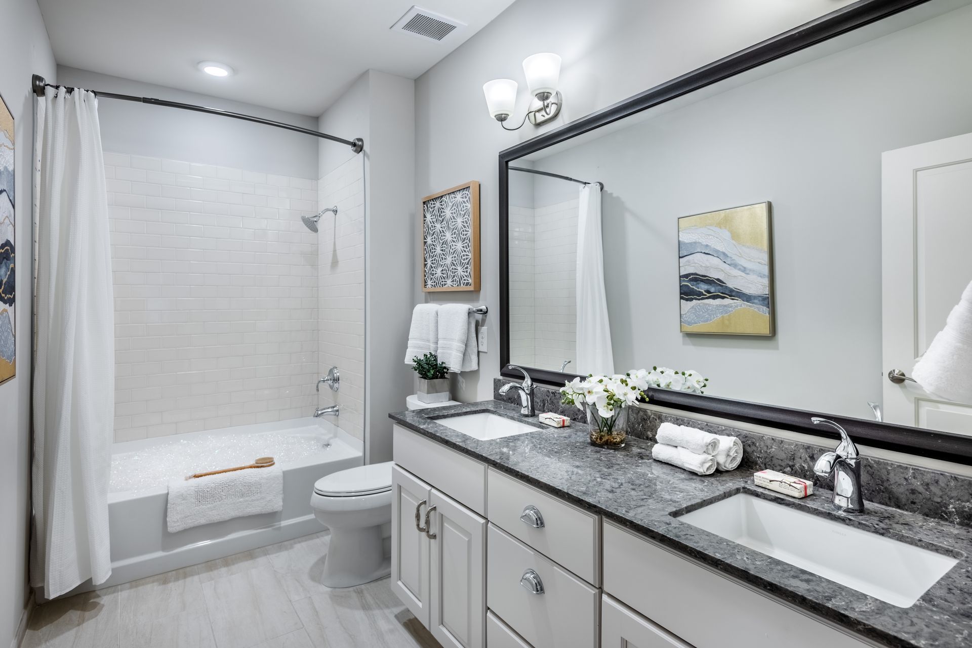Bathroom with white cabinetry, gray countertop, large mirror, and shower/tub combo.