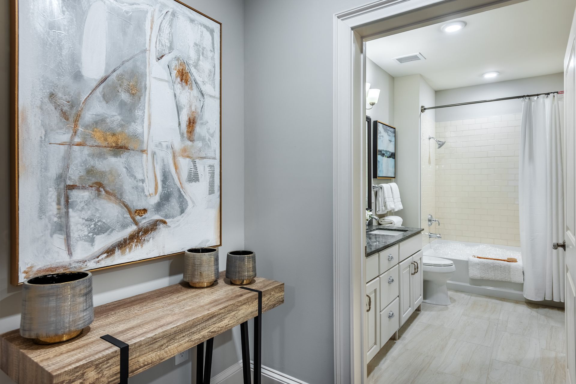 Hallway with artwork and console table, leading to a bathroom with a shower and vanity.