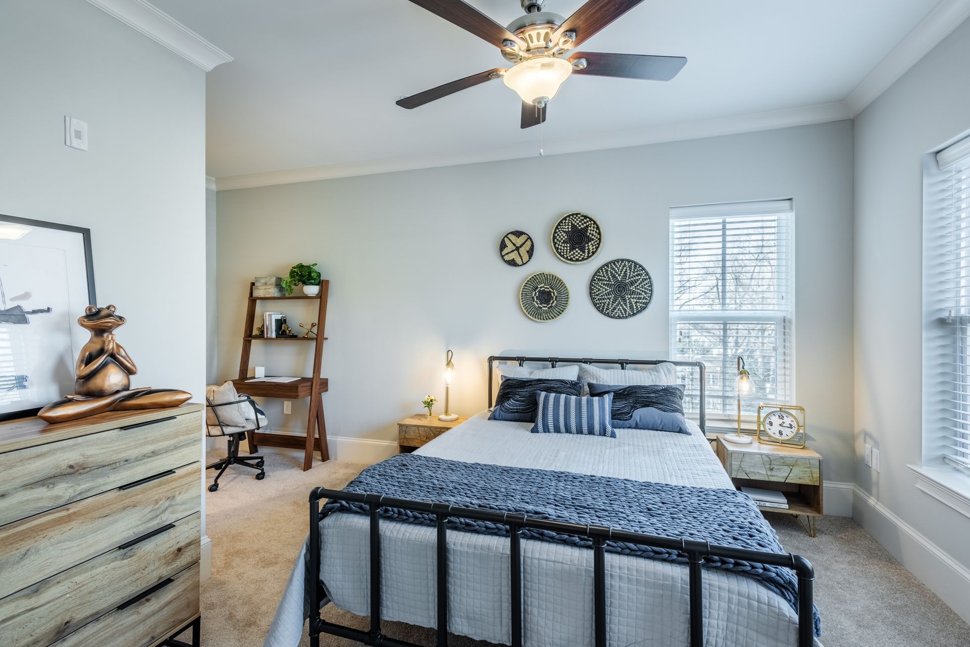 Bedroom with bed, desk, and decorative wall art. Pale gray walls, tan carpet.