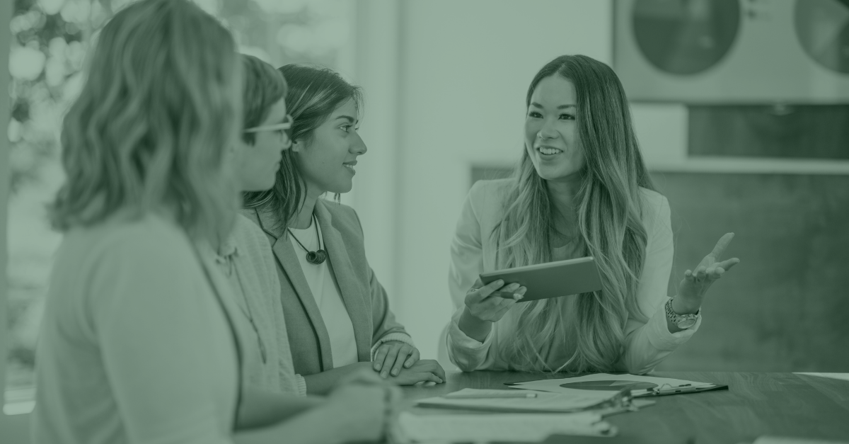 A group of women are sitting around a table having a meeting.