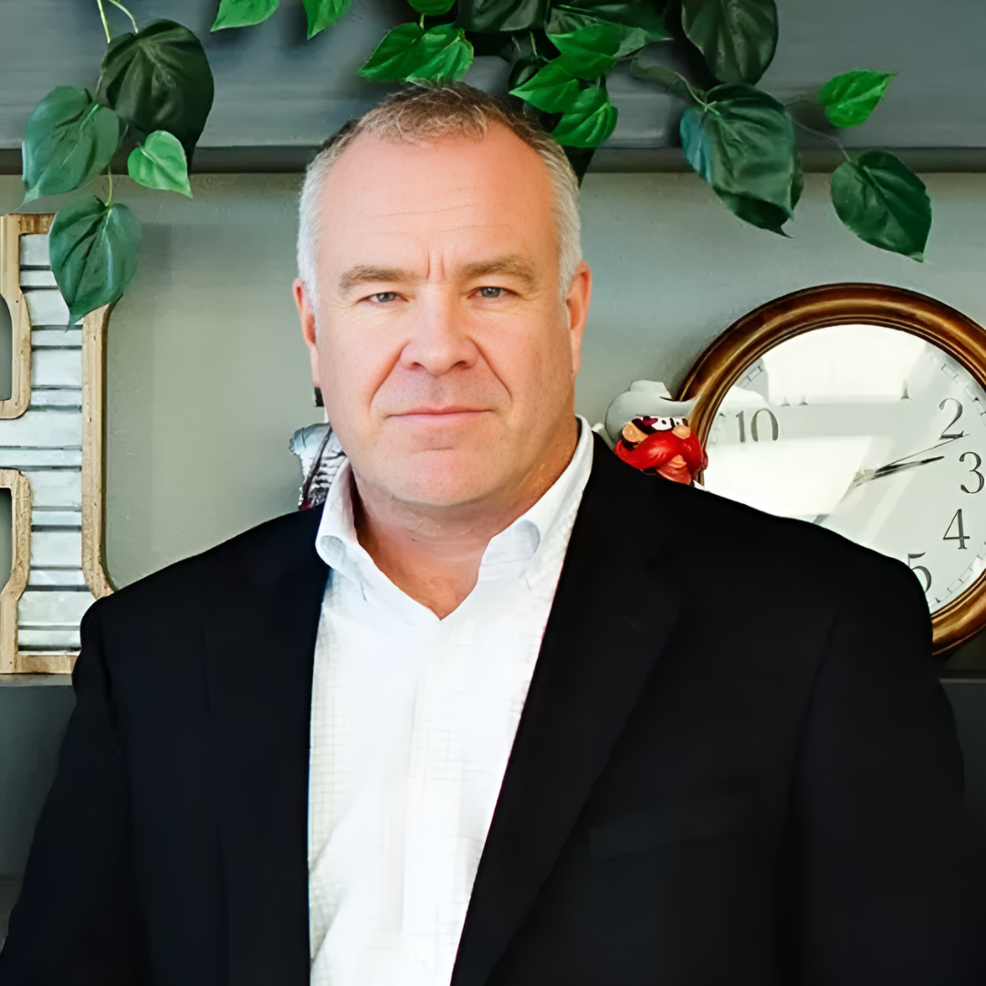 A man in a suit and white shirt is standing in front of a clock.