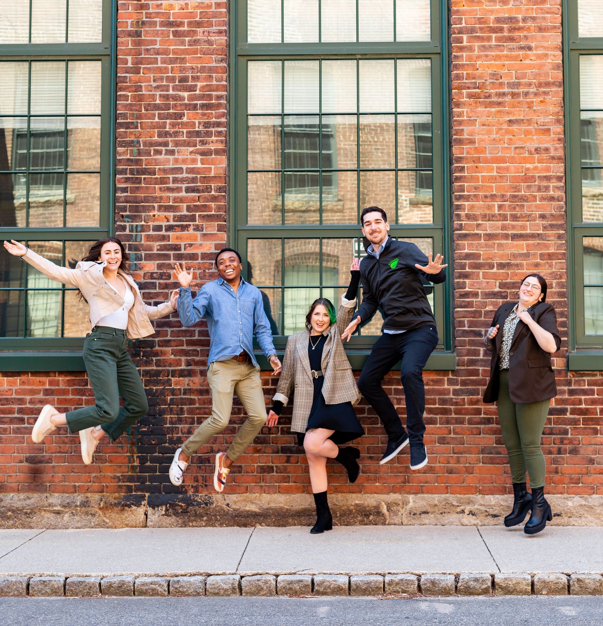 A group of people are jumping in the air in front of a brick building.