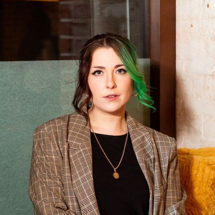 A woman with green hair is wearing a plaid jacket and a necklace