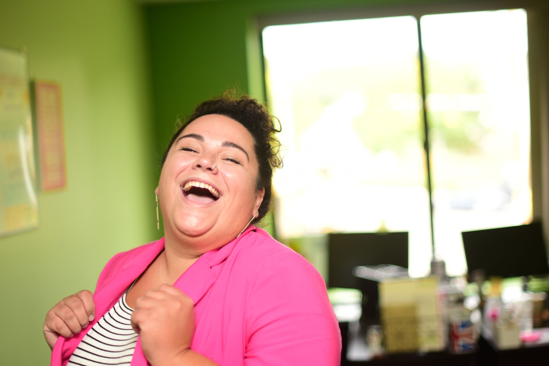 A woman in a pink jacket is laughing in a room.