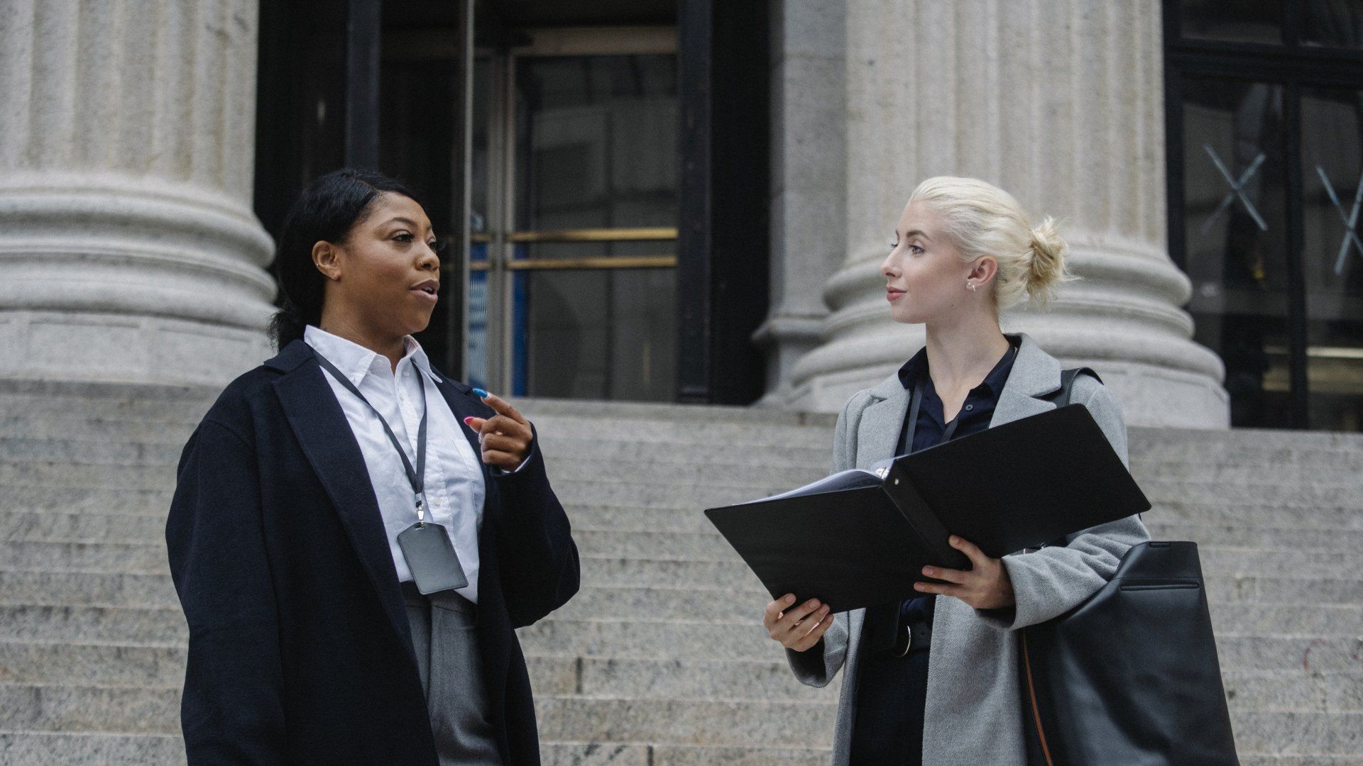 Two women are standing on the steps of a building talking to each other.