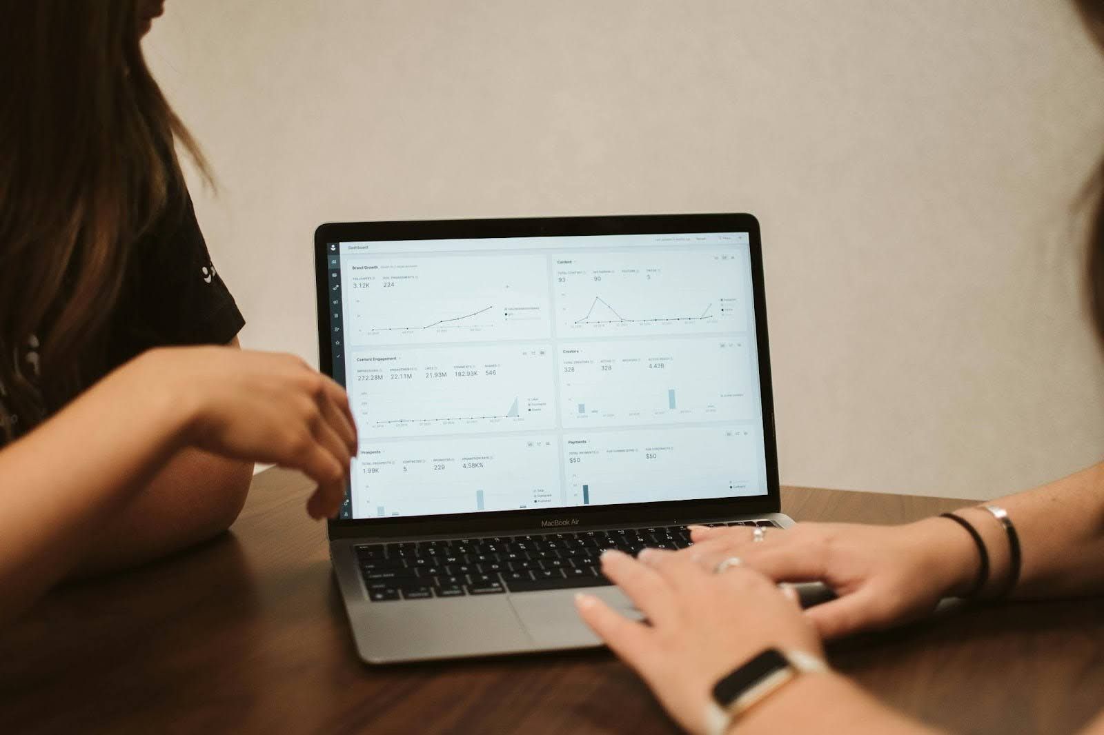 Two women are sitting at a table using a laptop computer.