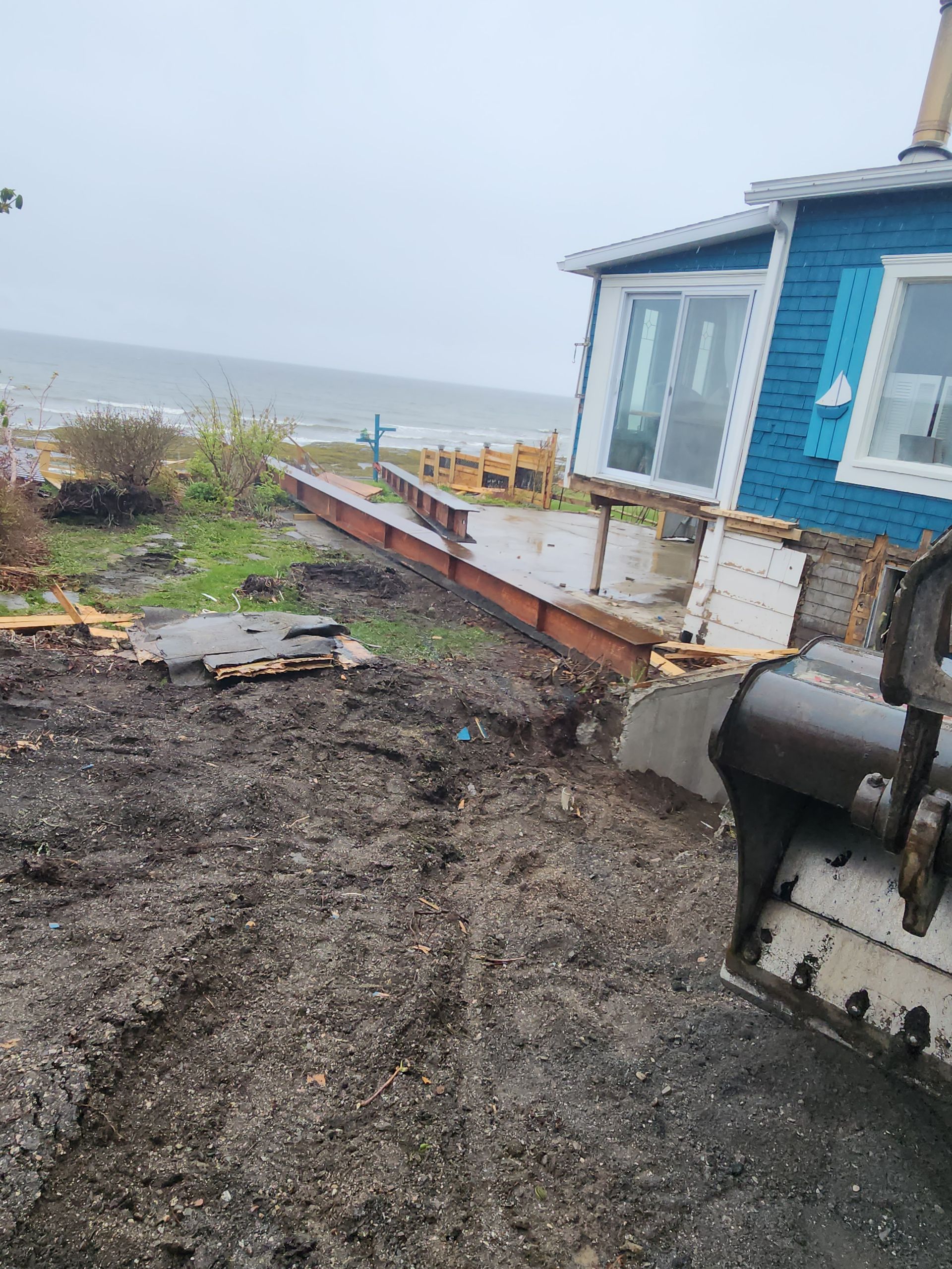 Une maison bleue est située au sommet d'un champ de terre à côté de l'océan.
