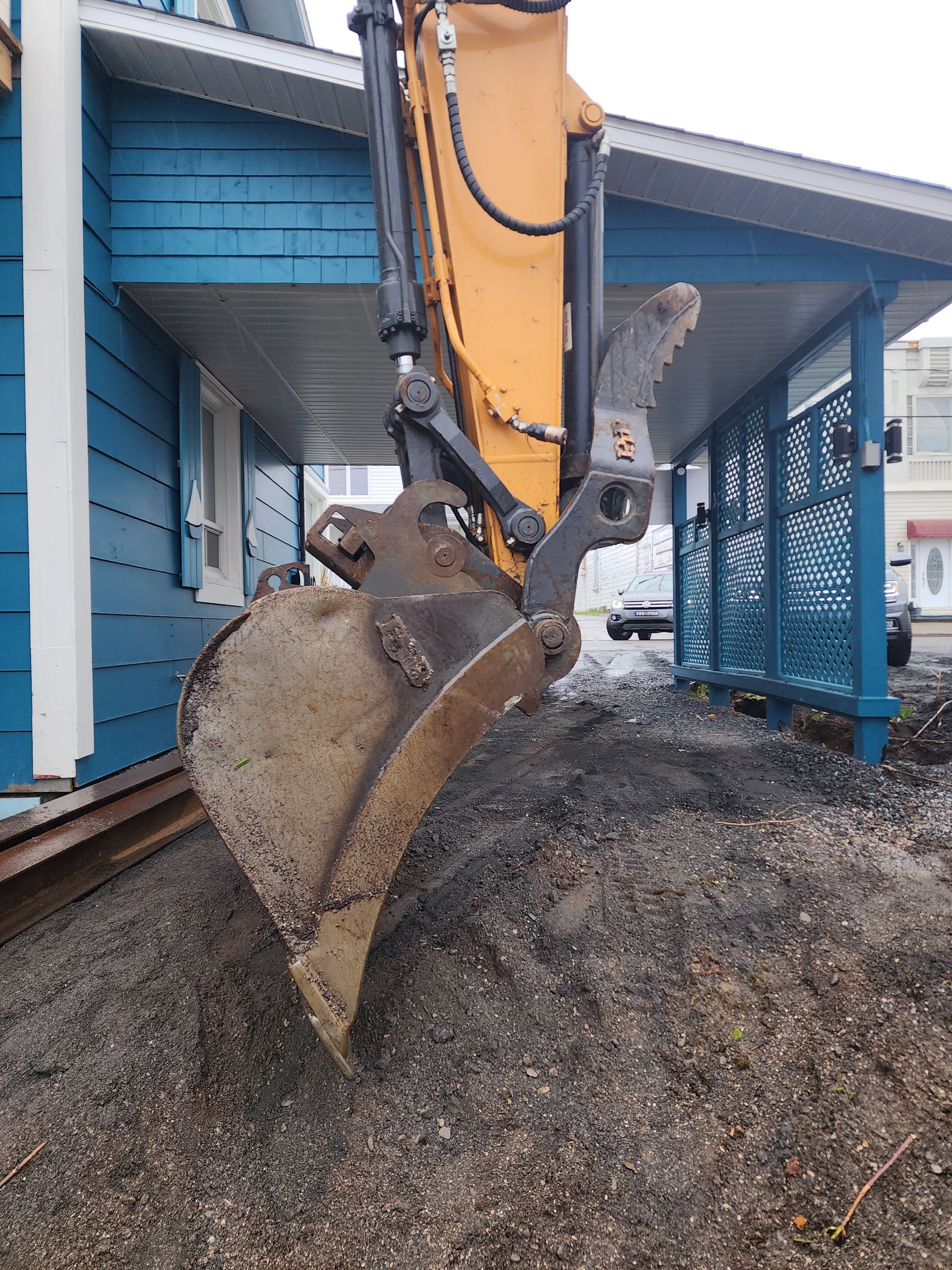 Une excavatrice creuse un trou devant une maison bleue.