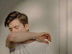 A young man is coughing into his elbow.