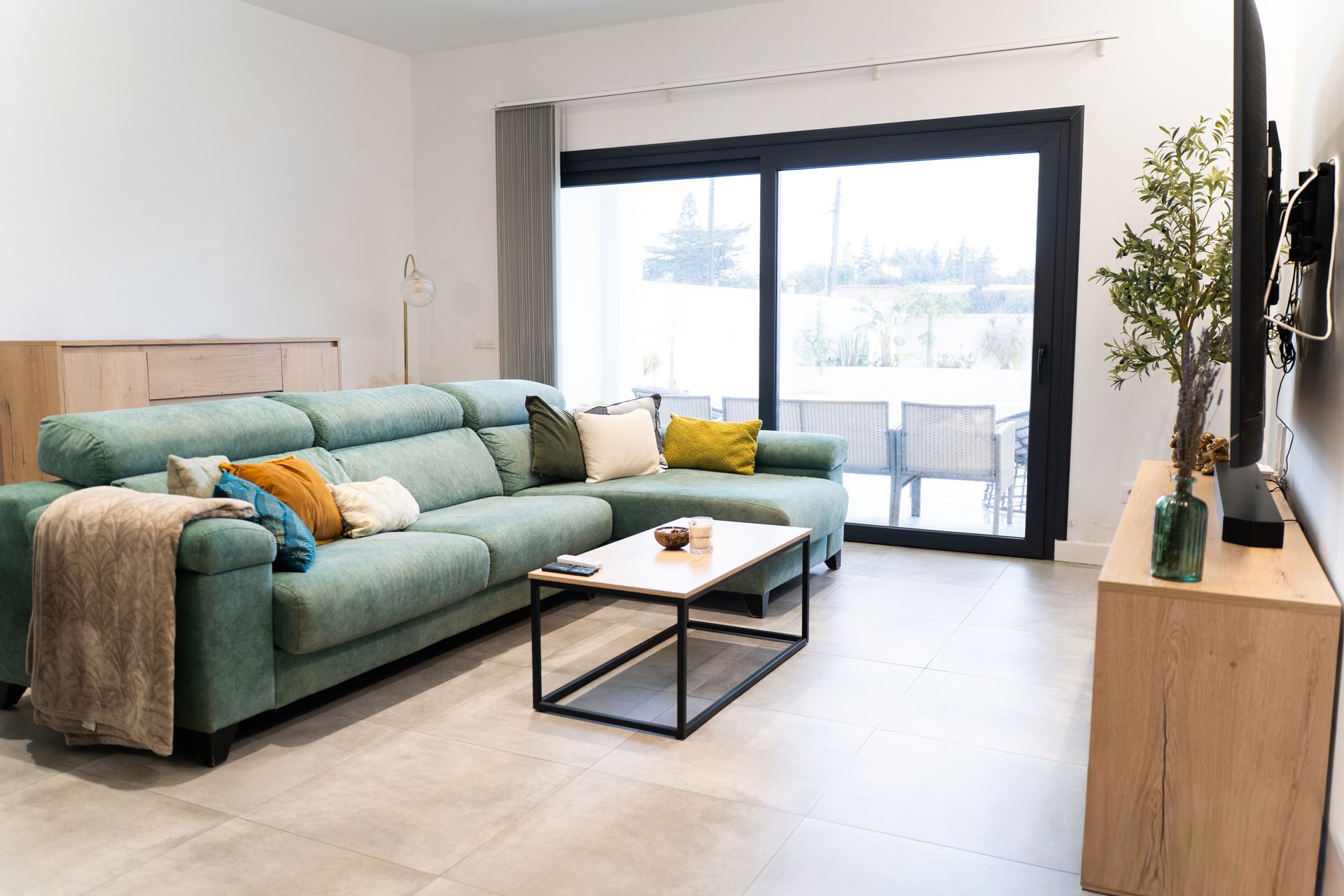 Modern living room with a teal sofa, large sliding glass doors, and a bright outdoor view. Modern living room with a teal sofa, large sliding glass doors, and a bright outdoor view.