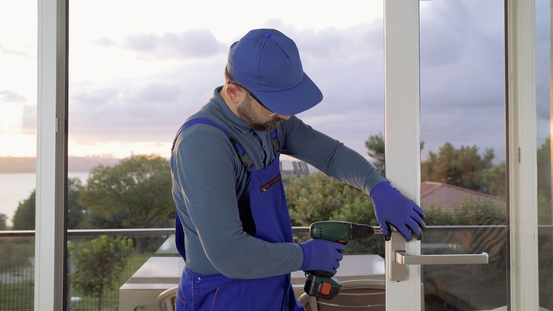 A man in blue overalls using a drill for professional glass door service maintenance work.