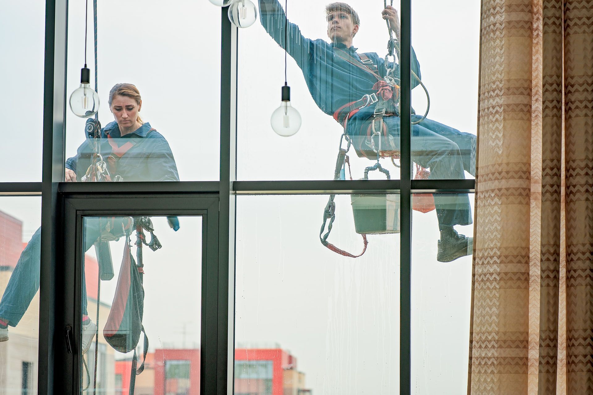 Technicians performing commercial window service using ropes and safety gear on glass façade. Technicians performing commercial window service using ropes and safety gear on glass façade.