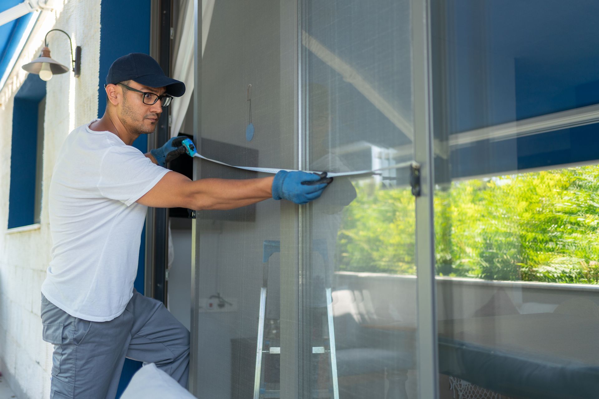 A man is cleaning a sliding glass door with a hose.