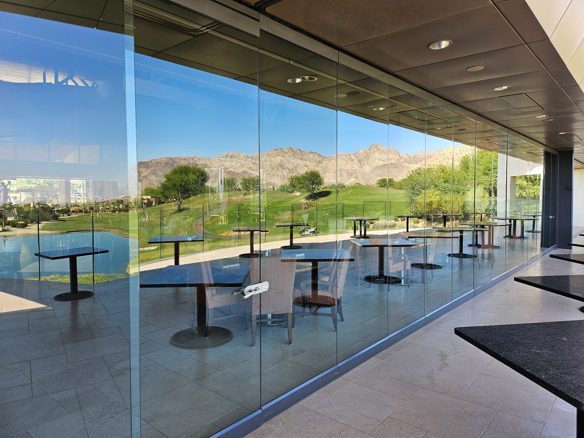 A room with tables and chairs in front of a glass wall.