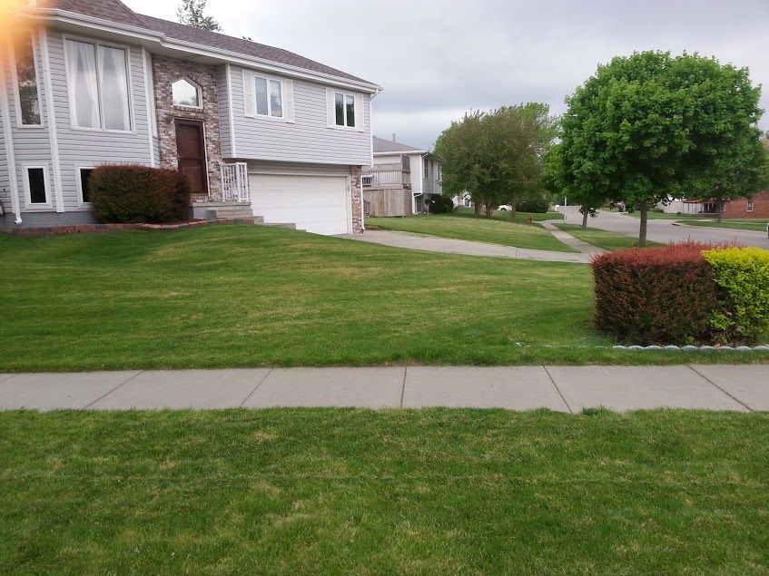 A green lawn mower is parked in the middle of a lush green lawn.