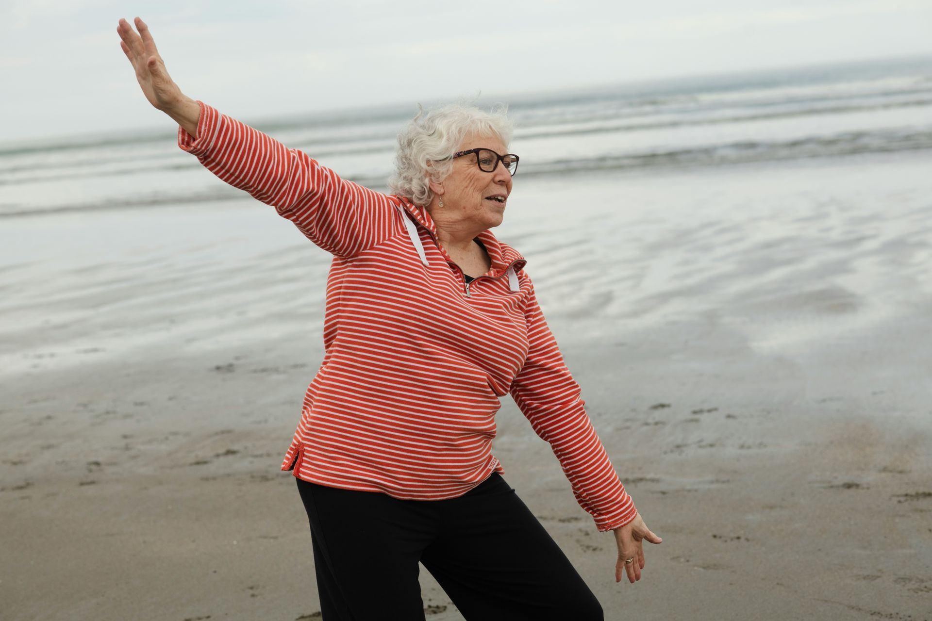 Woman in striped shirt practices Tai Chi on a beach.