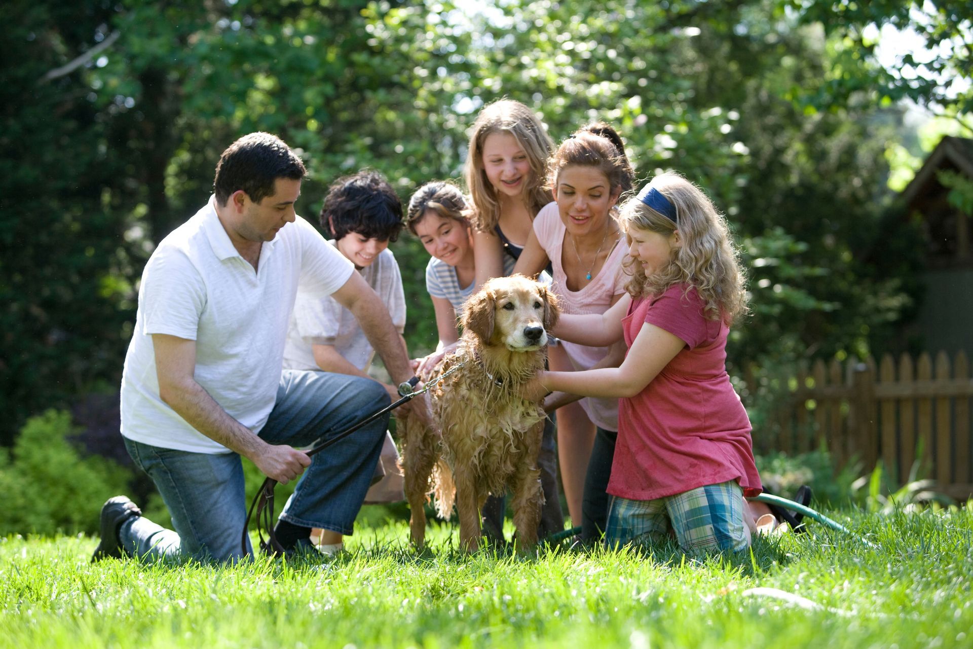 Family petting a wet golden retriever in a grassy yard.