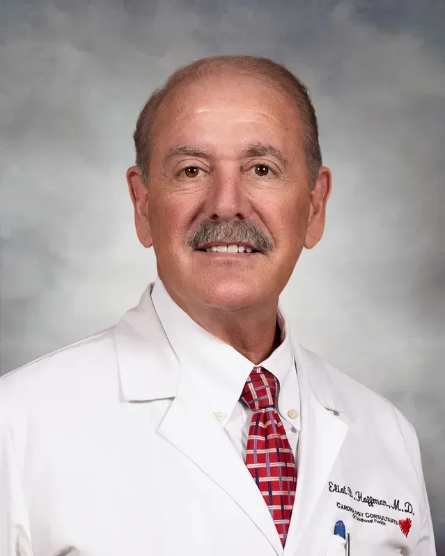 Man in a white lab coat with a red patterned tie, smiling.