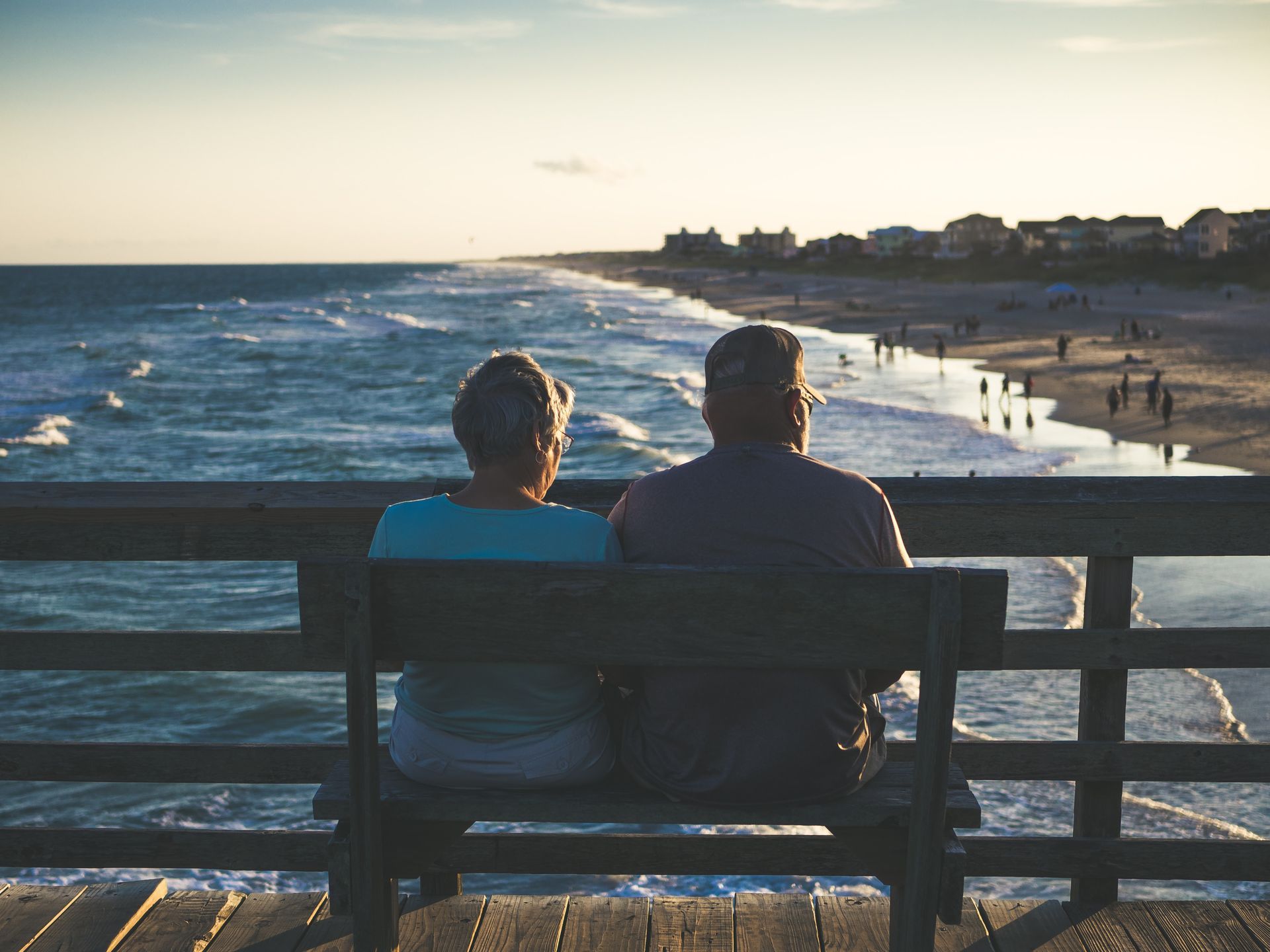 Couple sitting on bench, overlooking ocean at sunset.