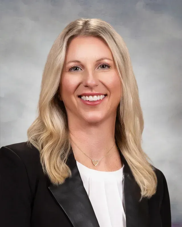 Woman with blonde hair wearing a black blazer and white shirt, smiling.