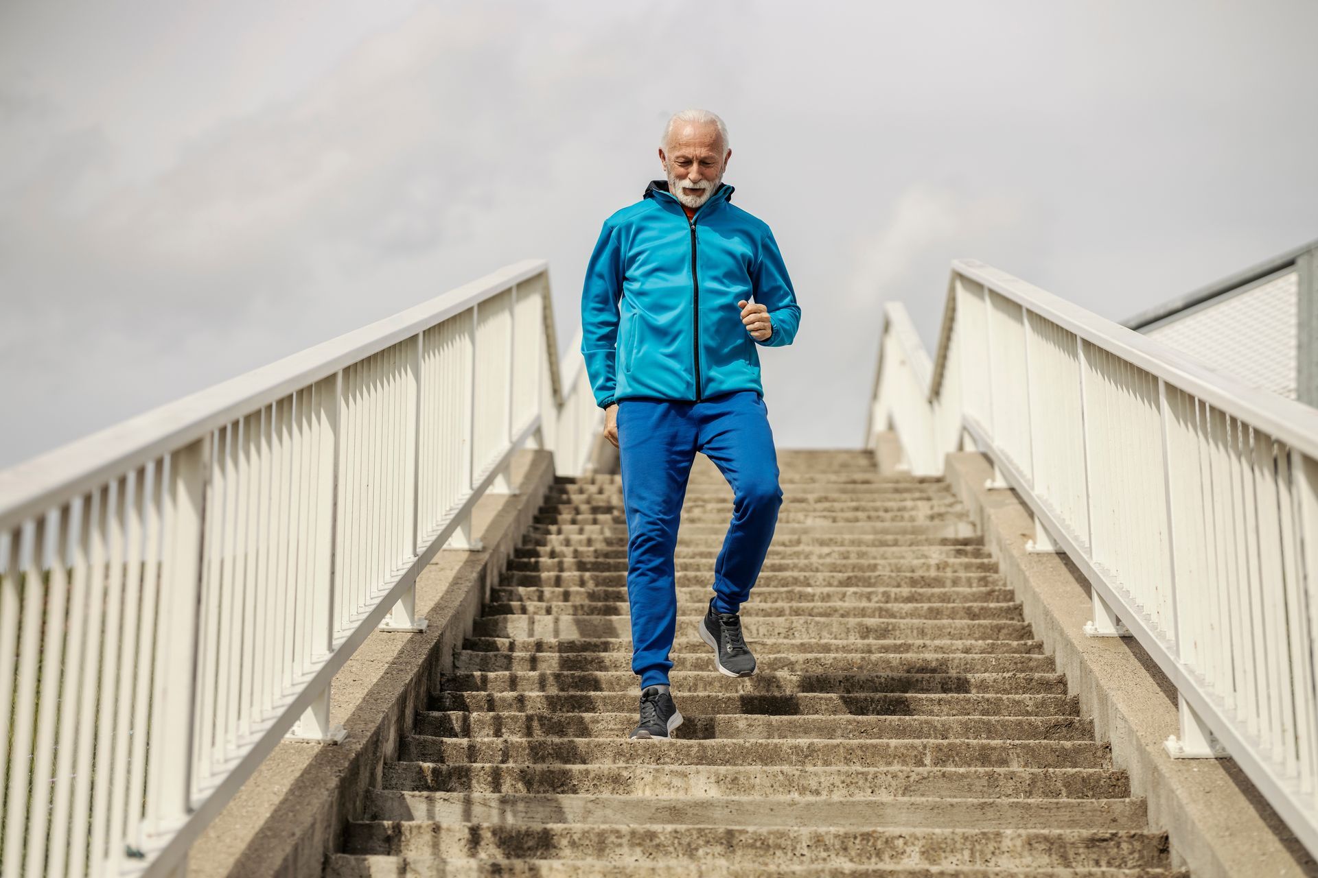 Man in blue sportswear descends outdoor concrete stairs.