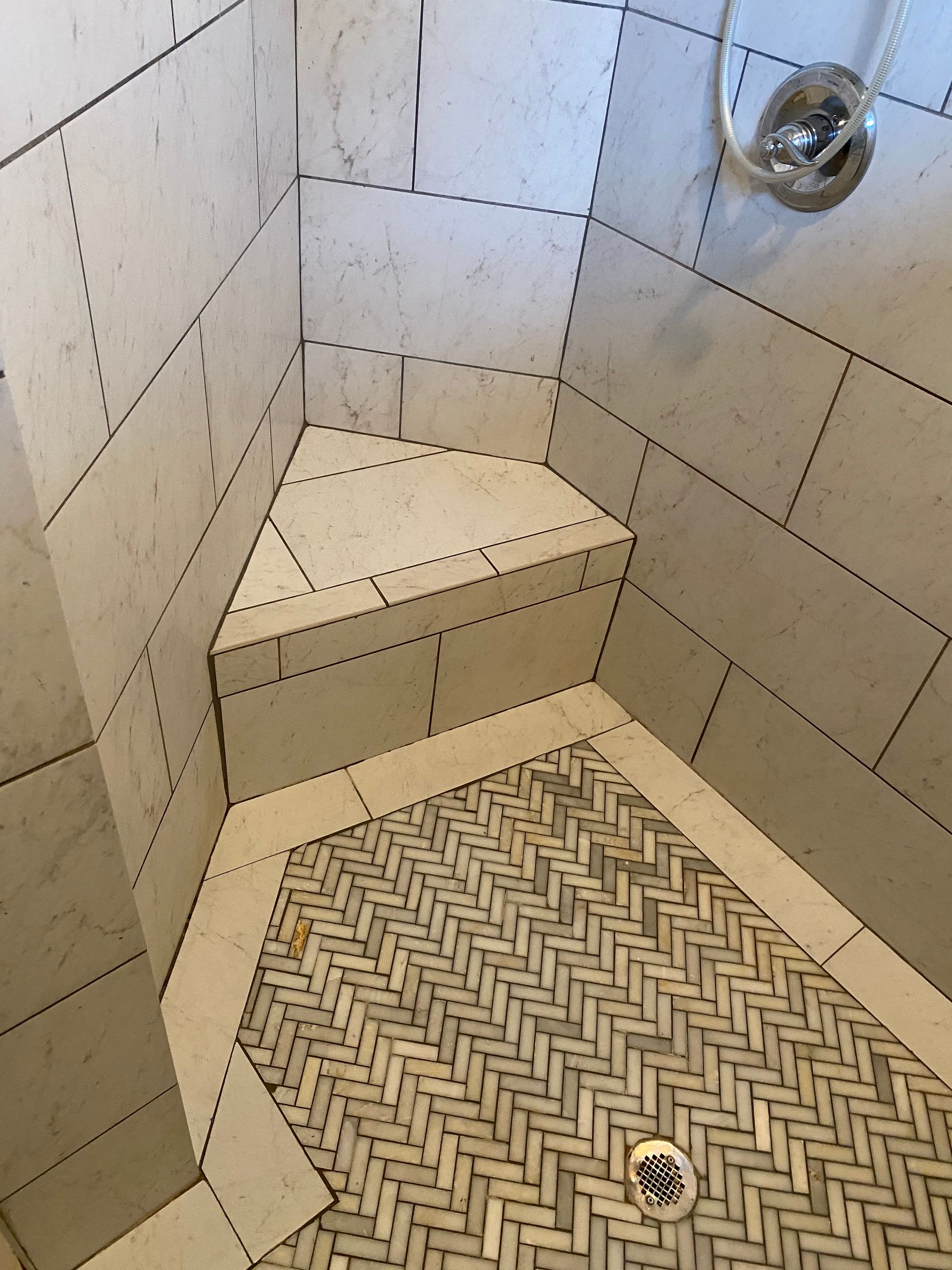 A shower with a corner seat and a drain