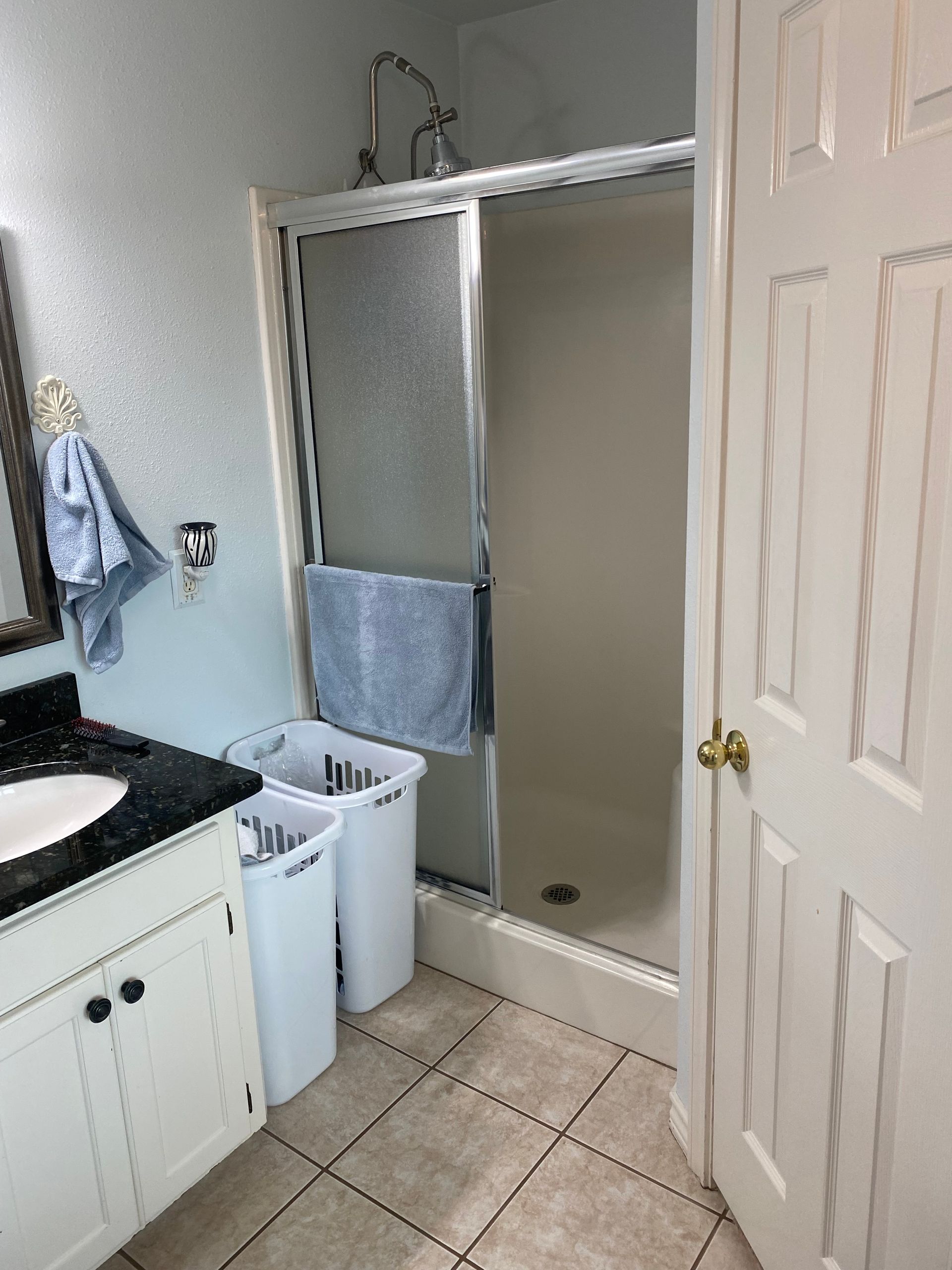 A bathroom with a sink , shower , and laundry baskets.