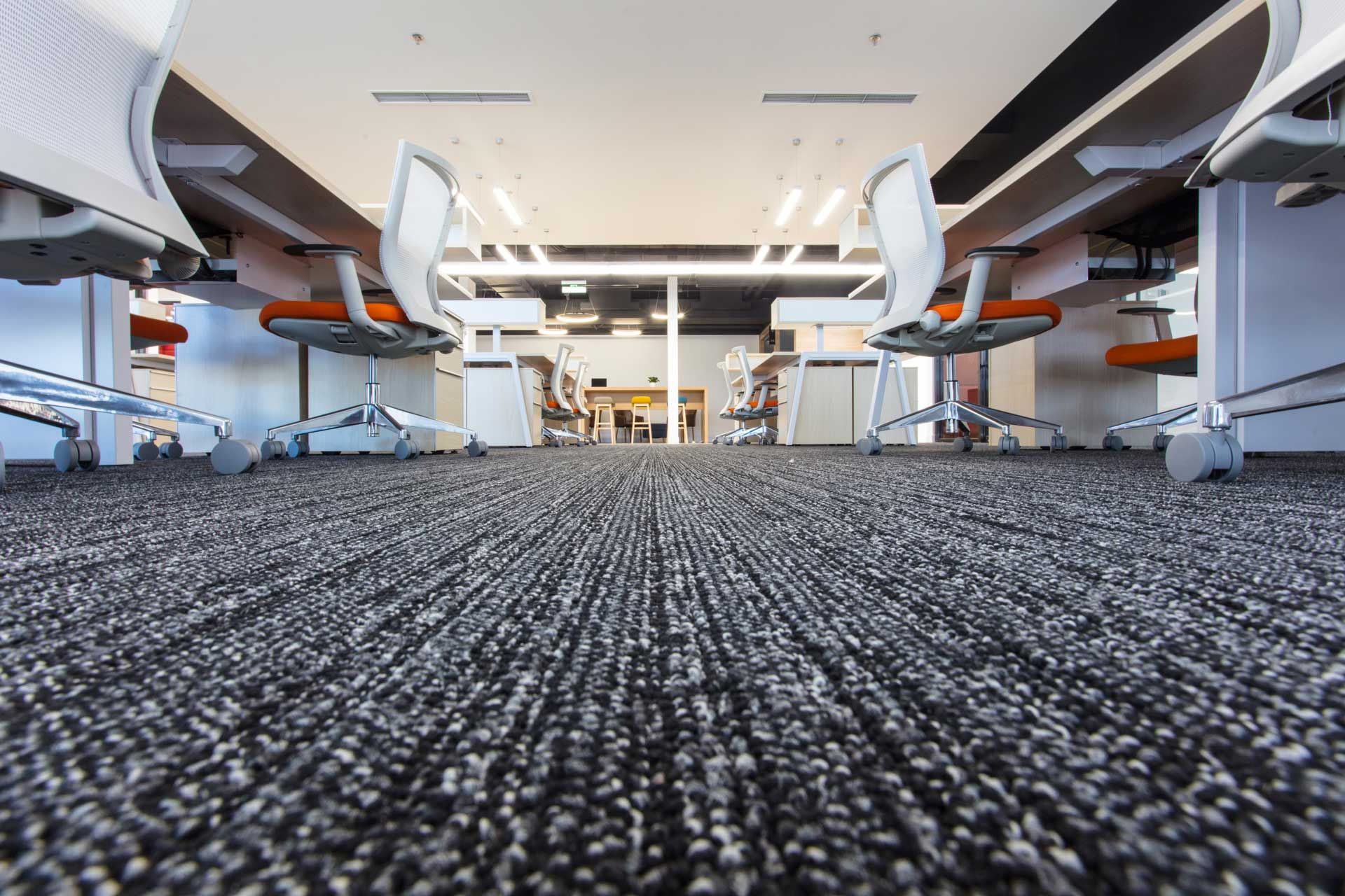 A close up of a carpeted floor in an office with desks and chairs.