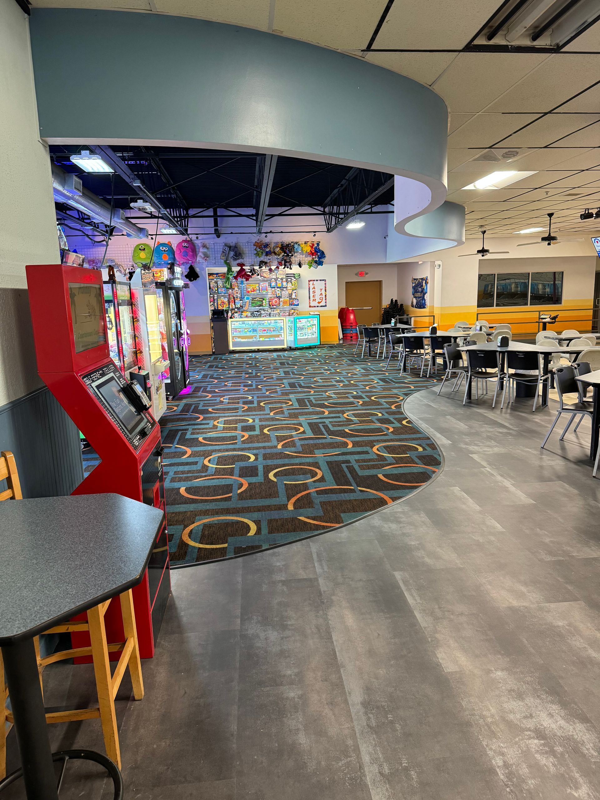 A large room with tables and chairs and a red arcade machine.