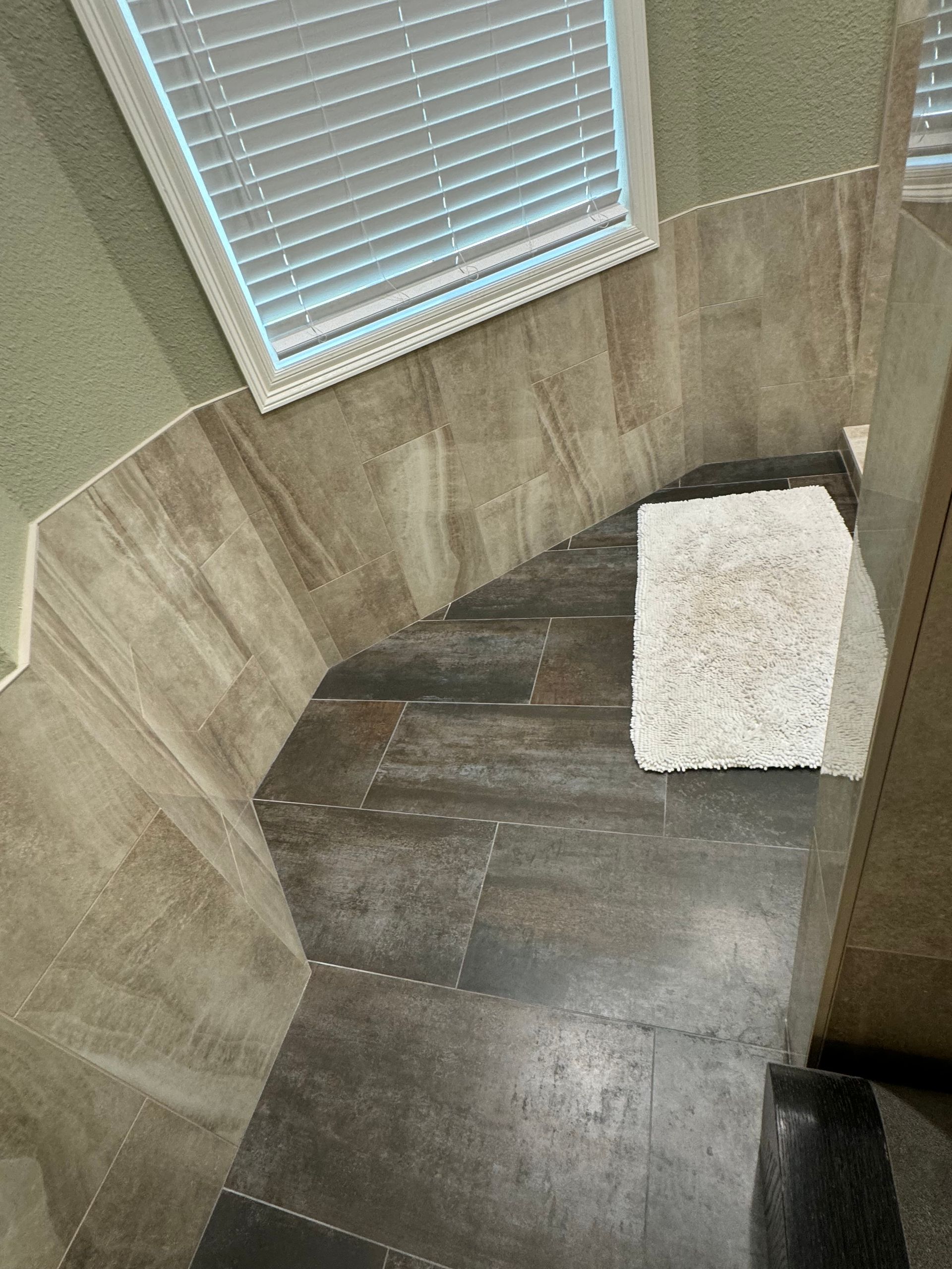 A bathroom with a rug on the floor and a window with blinds.