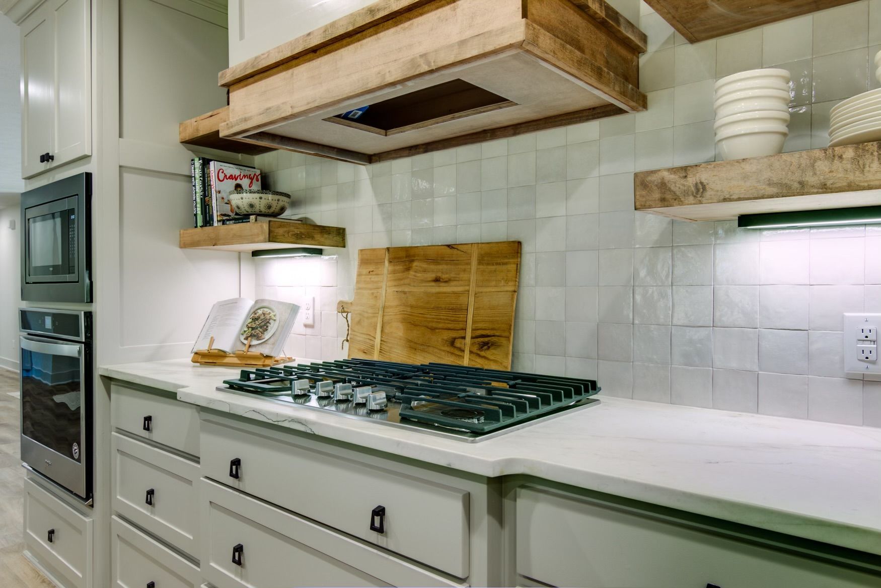 A kitchen with a stove top oven and a wooden cutting board on the counter.