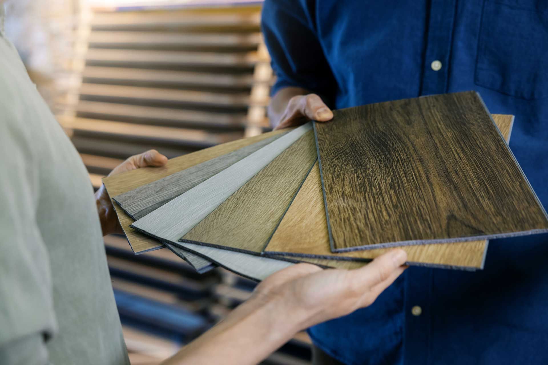 A man and a woman are holding samples of wooden flooring.