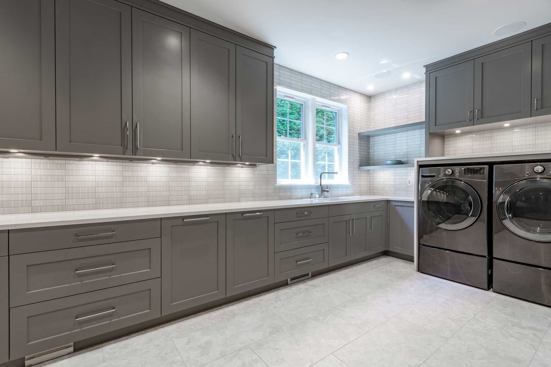 A laundry room with gray cabinets , a washer and dryer , and a window.
