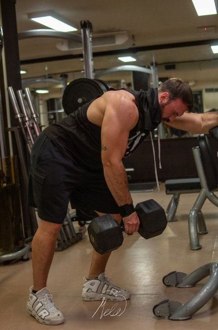 Nicola Voltolina in palestra, con indosso una canottiera nera, seduto con le mani giunte. Attrezzi da palestra visibili sullo sfondo.