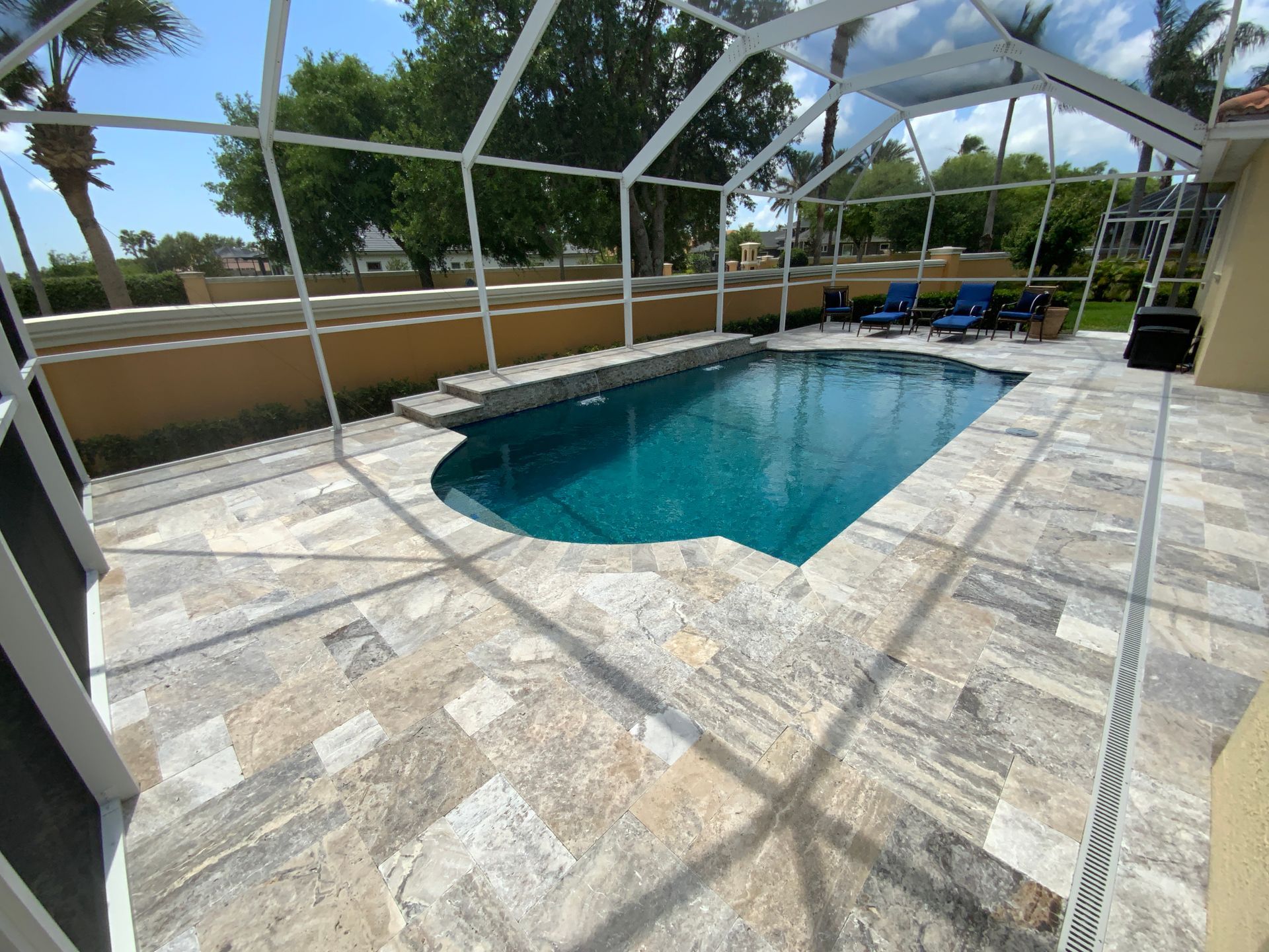 Pool with screened enclosure; stone patio, blue water, and lounge chairs.