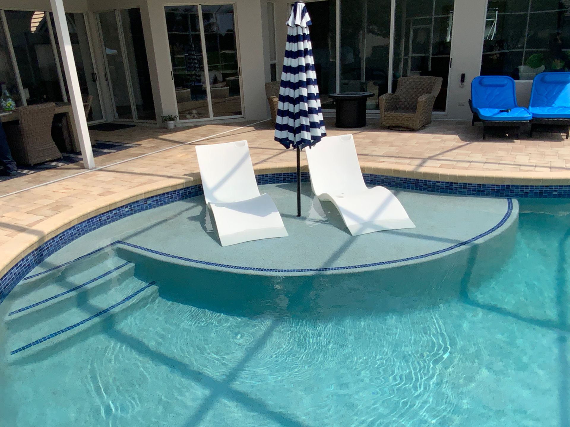 Pool with white lounge chairs, umbrella, and a blue tile border.