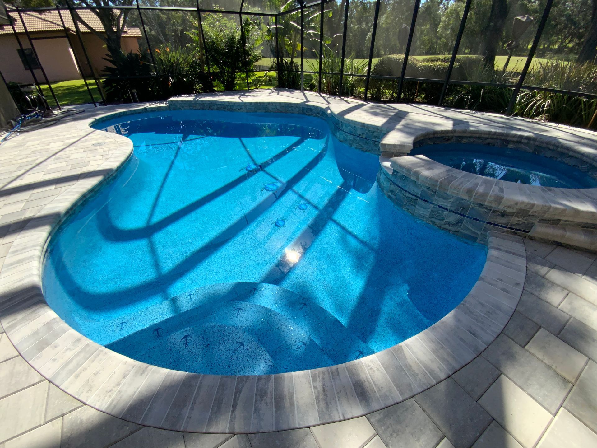 Pool with blue water and surrounding stone patio and hot tub, enclosed by a screen.