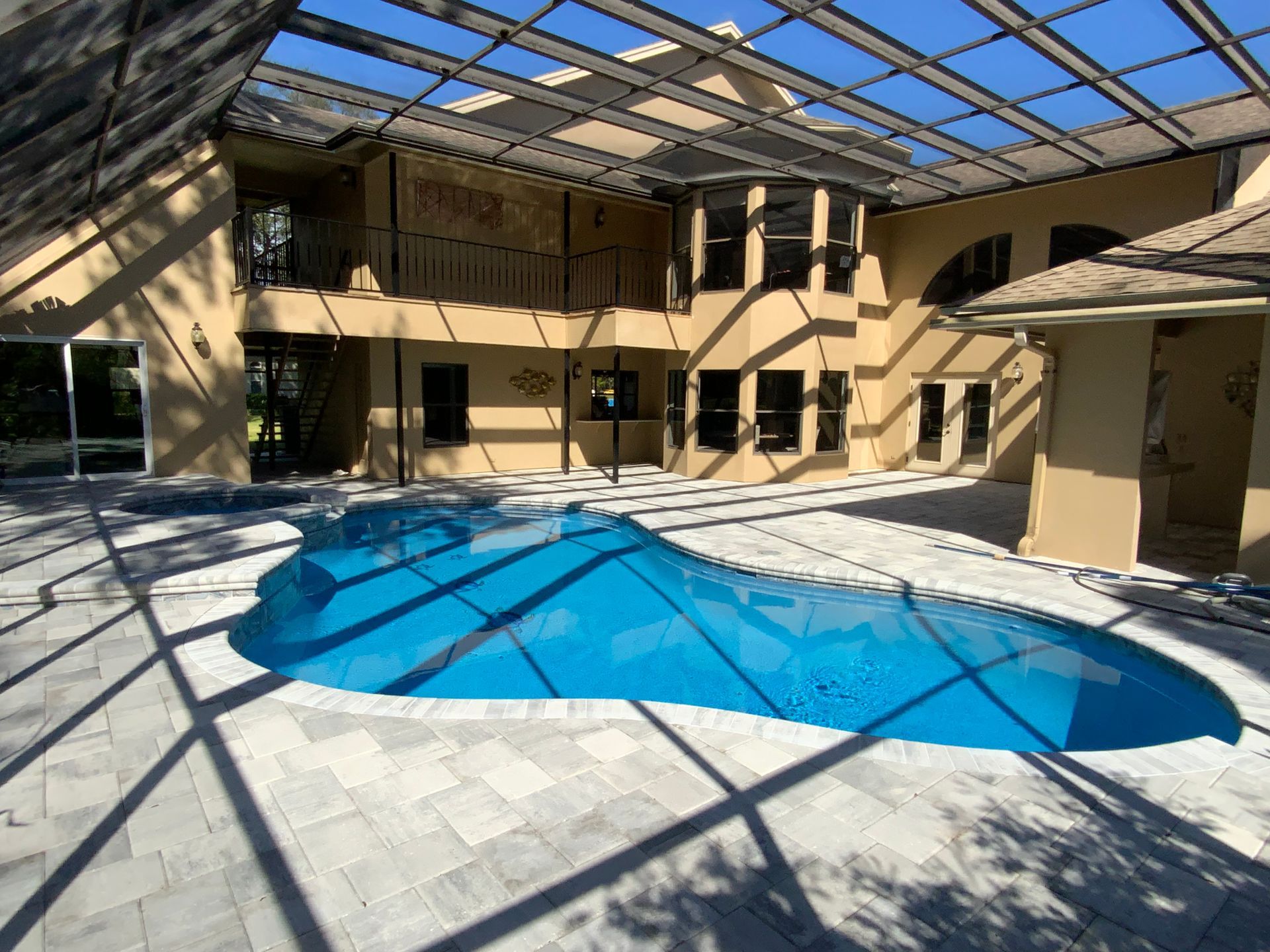 A large pool in a patio area, covered by a blue cover, enclosed by a beige house.
