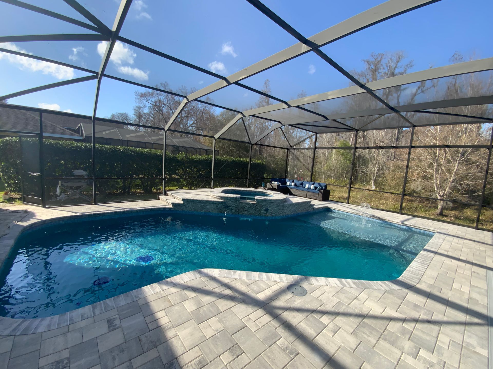 Pool and spa enclosed by a screened lanai with blue water, surrounded by brick patio.
