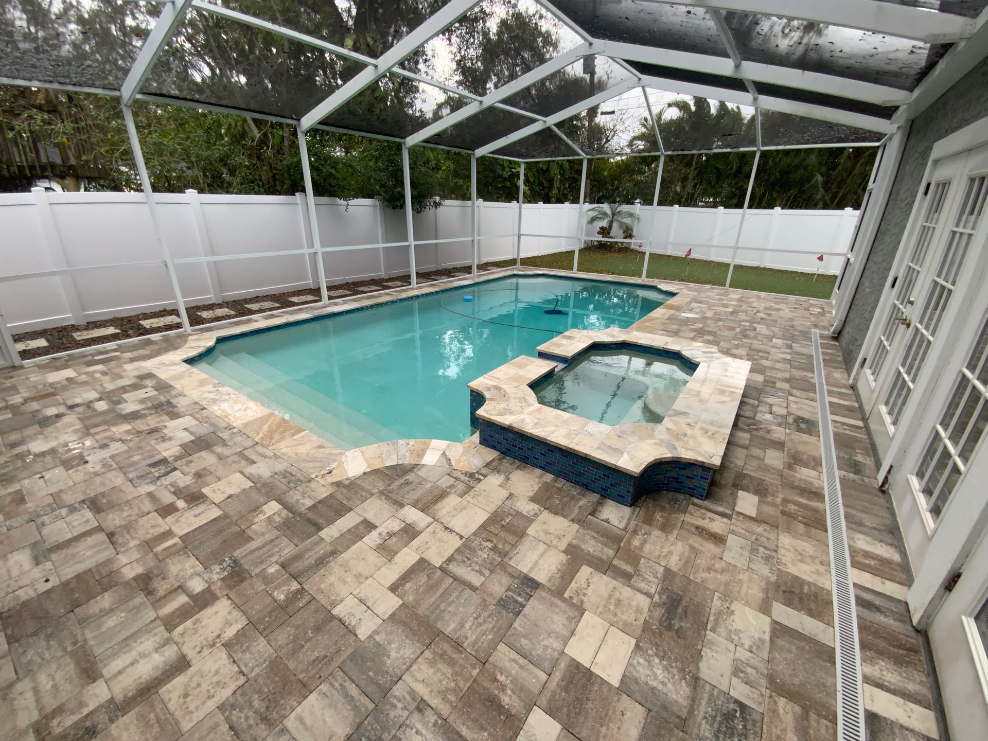 Pool and hot tub surrounded by paver patio, screened enclosure, and white fence.