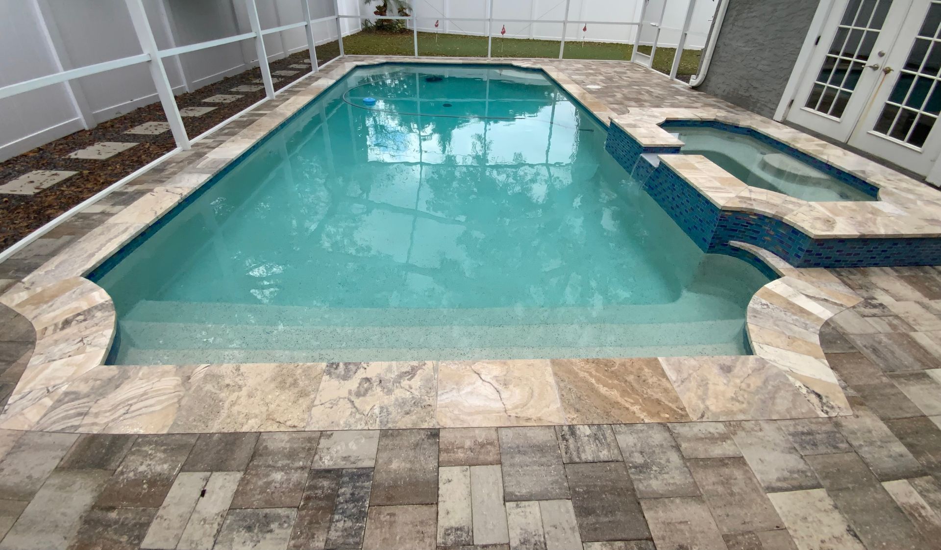 Swimming pool with attached jacuzzi and travertine patio.