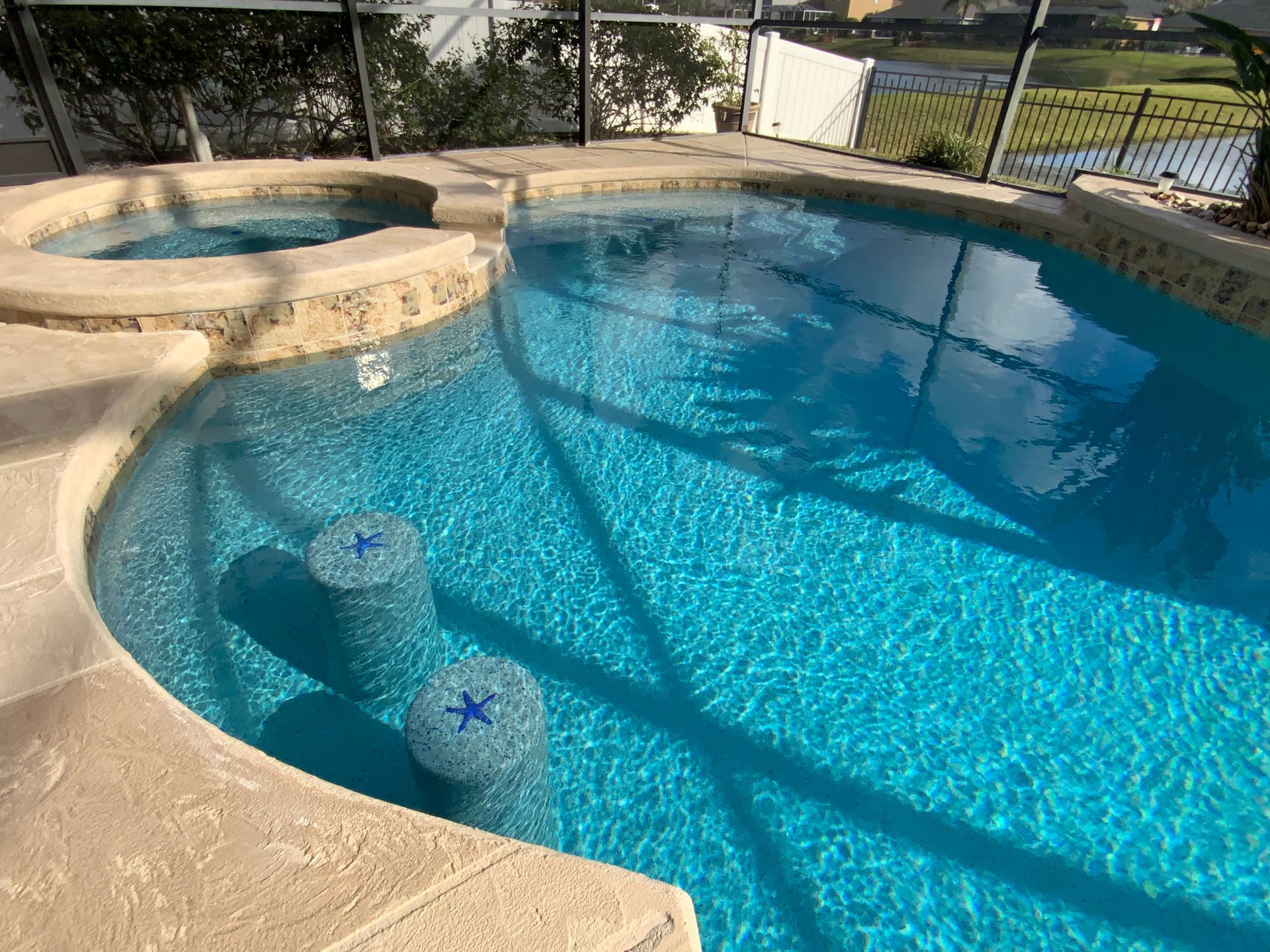 Swimming pool with built-in jacuzzi and swim-up bar stools. Bright blue water, tan coping, and a screened enclosure.